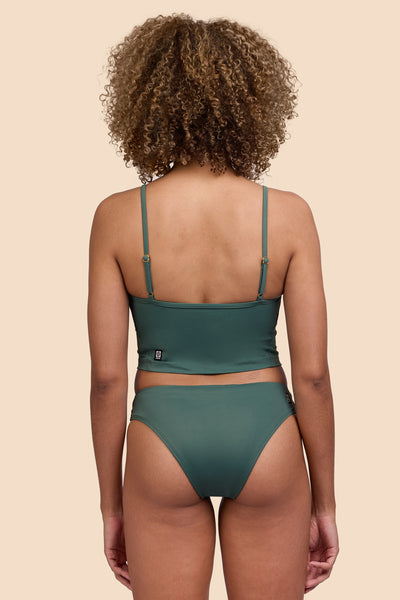 Female model wearing the Womens Gina Bikini Bottom in the Zucchini solid, standing in front of a yellow background shown from the back view

|| Size S, Hip 36"  