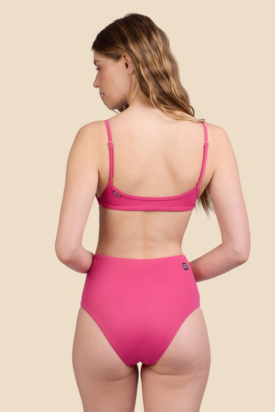 Female model wearing the Women's Janna Bikini Bottom in the Berry solid, standing in front of a yellow background shown from the back view

|| Size S, Hips 37"  
