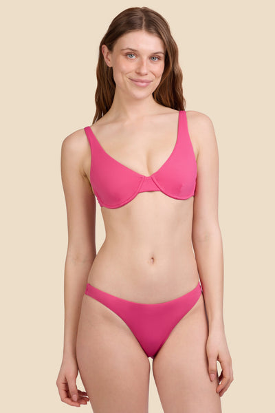 Female model wearing the Women's Kelia Bikini Bottom in the Berry solid, standing in front of a yellow background shown from the front view

|| Size S, Hips 37"  
