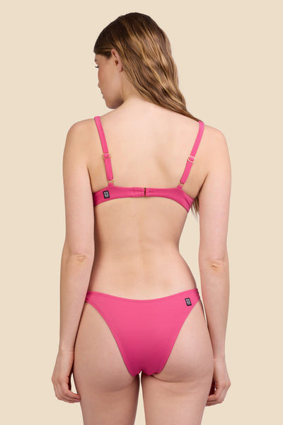 Female model wearing the Women's Kelia Bikini Bottom in the Berry solid, standing in front of a yellow background shown from the back view

|| Size S, Hips 37"  
