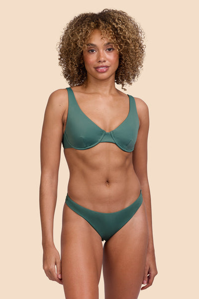 Female model wearing the Womens Kelia Bikini Bottom in the Zucchini solid, standing in front of a yellow background shown from the front view

|| Size S, Hip 36"  
