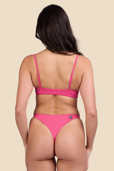 Female model wearing the Women's Odessa Bikini Bottom in the Berry solid, standing in front of a yellow background shown from the back view

|| Size S, Hips 34"  

