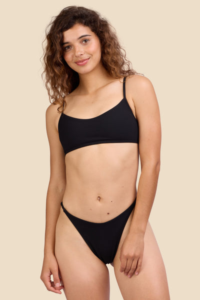Female model wearing the Women's Odessa Bikini Bottom in the Black Ribbed solid, standing in front of a yellow background shown from the front view

|| Size S, Hips 39"  
