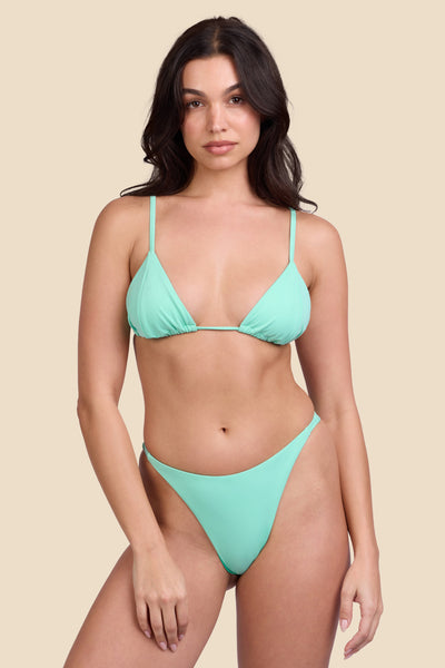 Female model wearing the Women's Odessa Bikini Bottom in the Mint Tulip solid, standing in front of a yellow background shown from the front view

|| Size S, Hips 34"  
