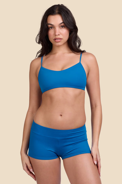 Female model wearing the Women's Piha Surf Short in the Blue Moon solid, standing in front of a yellow background shown from the front view

|| Size S, Hips 34"  
