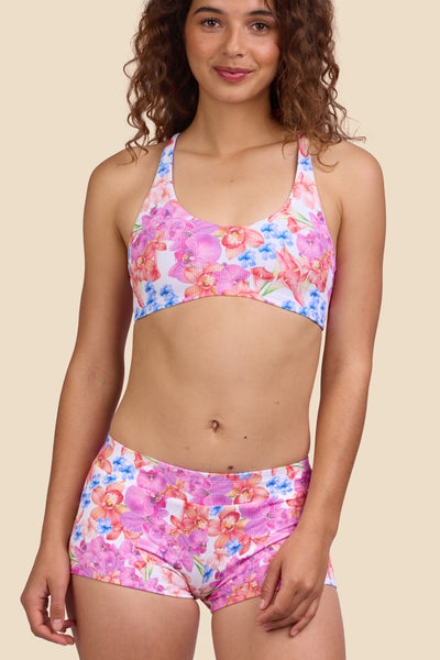 Female model wearing the Women's Piha Surf Short in the Orchids Ribbed print, standing in front of a yellow background shown from the front view

|| Size S, Hips 39" 