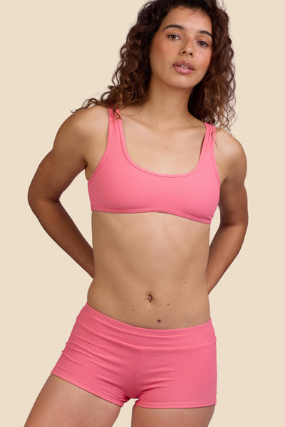 Female model wearing the Women's Piha Surf Short in the Tea Rose Ribbed solid, standing in front of a yellow background shown from the front view

|| Size S, Hips 39"  