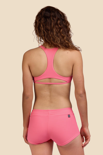 Female model wearing the Women's Piha Surf Short in the Tea Rose Ribbed solid, standing in front of a yellow background shown from the back view

|| Size S, Hips 39"  