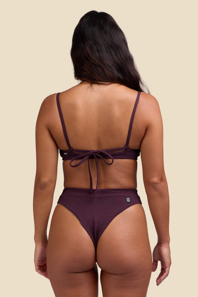 Female model wearing the Women's Sirena Bikini Bottom in the Sangria solid, standing in front of a yellow background shown from the back view

|| Size S, Hips 35"  