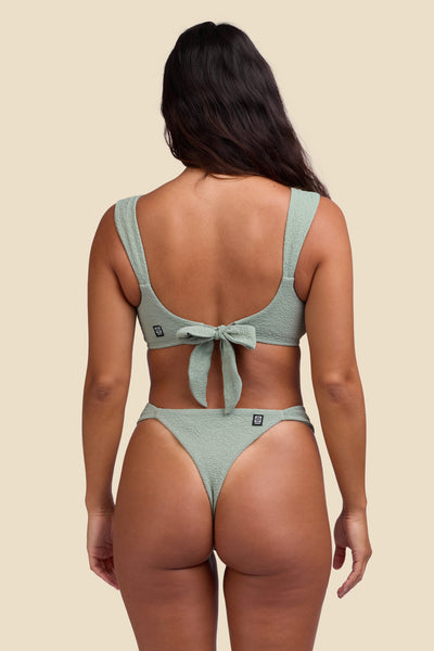 Female model wearing the Women's Suri Bikini Bottom in the Algae solid, standing in front of a yellow background shown front the back view

|| Size S, Hip 35"  