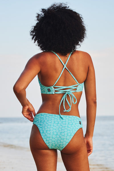 Female model wearing the Women's Valle Bikini Bottom in the Clamshell Ribbed print, standing in front of a beach shown from the back view
