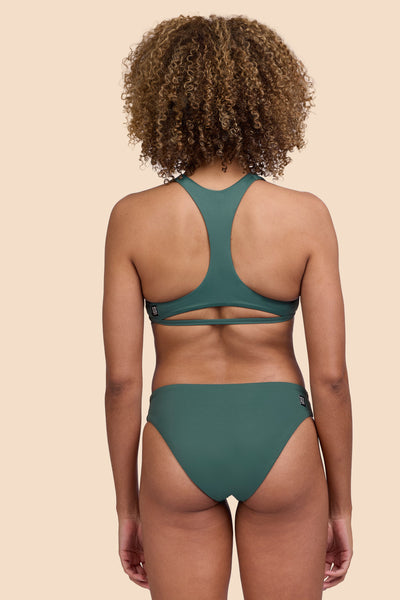 Female model wearing the Womens Valle Bikini Bottom in the Zucchini solid, standing in front of a yellow background shown from the back view

|| Size S, Hip 36"  