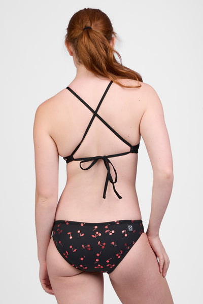 Female model wearing the Women’s Andy Bikini Bottom in the Cherry Burst print, standing in front of a grey background, shown from back view. 