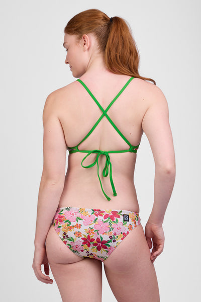 Female model wearing the Women’s Andy Bikini Bottom in the Sunset Luau print, standing in front of a grey background, shown from back view. 
