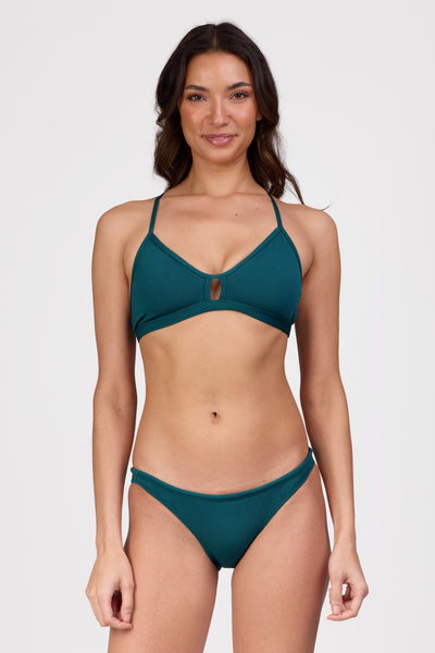 Female model wearing the Women's Brazil Bikini Bottom in the Peacock solid, standing in front of a grey background shown from the front view

|| Size S, Hips 36 1/2"  

