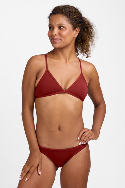 Female model wearing the Women’s Europe Bikini Bottom in the Paprika solid, standing in front of a grey background, shown from front view. 
