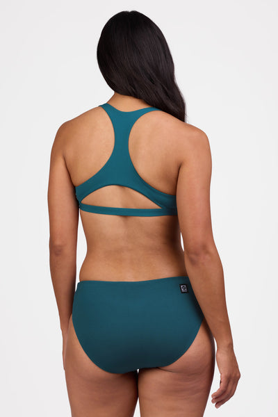 Female model wearing the Women's Sandra Bikini Bottom in the Peacock solid, standing in front of a grey background shown from the back view


|| Size M, Hips 40"
