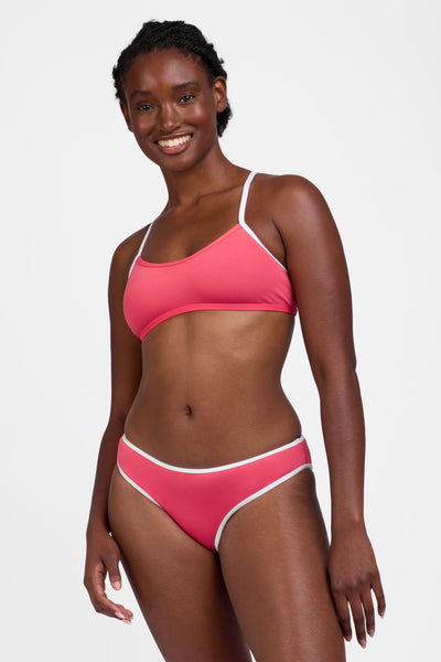 Male model wearing the Women's Whitney Bikini Bottom in the Guava Crush contrast, standing in front of a grey background, shown from the front view

|| Size M, Hips 35"  