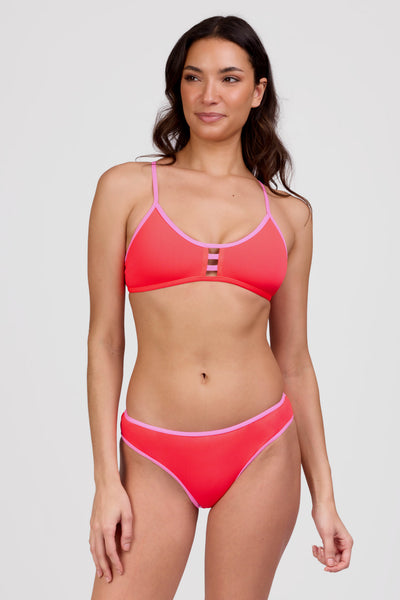 Female model wearing the Women's Whitney Bikini Bottom in the Neon Guava contrast, standing in front of a grey background shown from the front view

|| Size S, Hips 36 1/2"  
