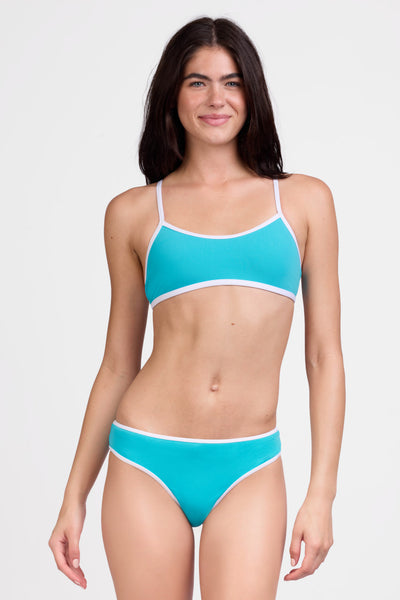 Female model wearing the Women's Whitney Bikini Bottom in the Sky Blue contrast, standing in front of a grey background shown from the front view

|| Size S, Hips 35"