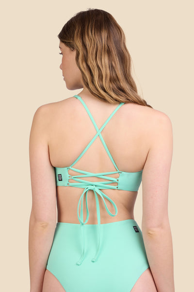 Female model wearing the Women's Blake Bikini Top in the Mint Tulip solid, standing in front of a yellow background shown from the back view

|| Size S, Bust 30.5"  
