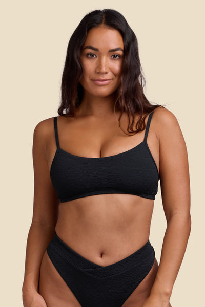 Female model wearing the Women's Delphine Bikini Top in the Black solid, standing in front of a yellow background shown from the front view

|| Size S, Bust 34"  