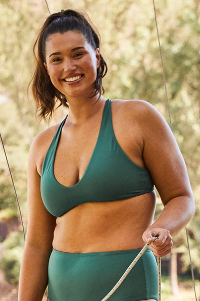 Female model wearing the Womens Doris Bikini Top in the Zucchini solid, standing in front of a green background shown from the front view