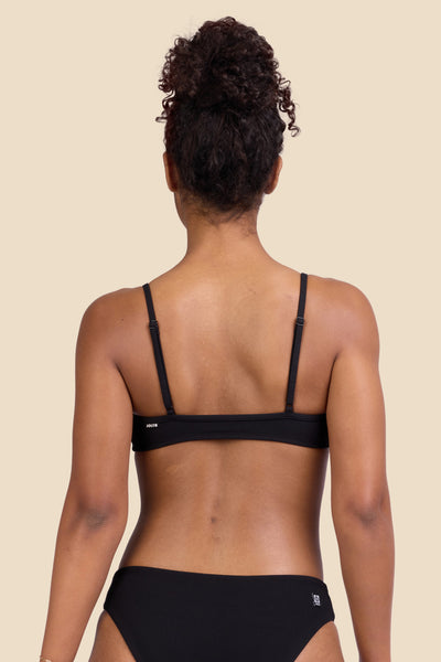 Female model wearing the Women's Eryn Bikini Top in the Black Ribbed solid, standing in front of a yellow background shown from the back view

|| Size S, Bust 32"  