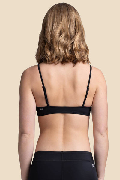 Female Model wearing the Women's Eryn Bikini Top in the Black solid, standing in front of a yellow background, shown from the back view