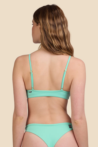 Female model wearing the Women's Faye Bikini Top in the Mint Tulip solid, standing in front of a yellow background shown from the back view

|| Size S, Bust 30.5"  
