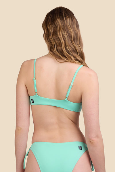 Female model wearing the Women's Jenny Bikini Top in the Mint Tulip solid, standing in front of a yellow background shown from the back view

|| Size S, Bust 30.5"  
