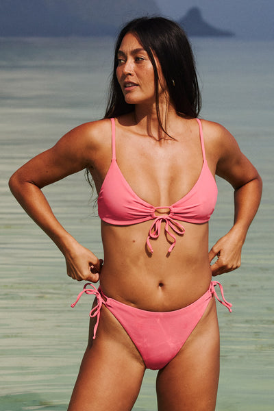 Female model wearing the Women's Jenny Bikini Top in the Tea Rose Ribbed solid, standing in front of the ocean shown from the front view