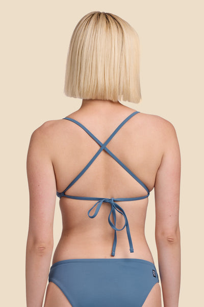 Female model wearing the Women's Lily Bikini Top in the Dolphins solid, standing in front of a yellow background shown from the back view


