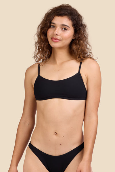 Female model wearing the Women's Lori Bikini Top in the Black Ribbed solid, standing in front of a yellow background shown from the front view

|| Size S, Bust 35.5"  