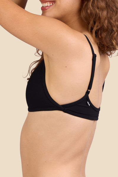 Female model wearing the Women's Lori Bikini Top in the Black Ribbed solid, standing in front of a yellow background shown from the side view

|| Size S, Bust 35.5"  