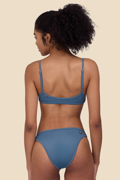 Female model wearing the Women's Lori Bikini Top in the Dolphins solid, standing in front of a yellow background shown from the back view


