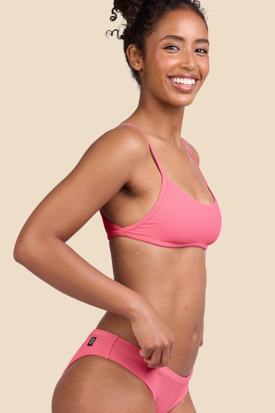 Female model wearing the Women's Lori Bikini Top in the Tea Rose Ribbed solid, standing in front of a yellow background shown from the side view

|| Size S, Bust 32"  