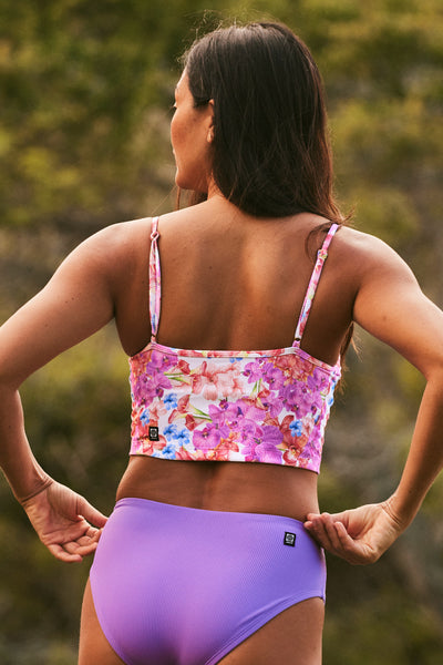 Female model wearing the Women's Luca Tankini Top in the Orchids Ribbed print, standing in front of a green background shown from the back view
