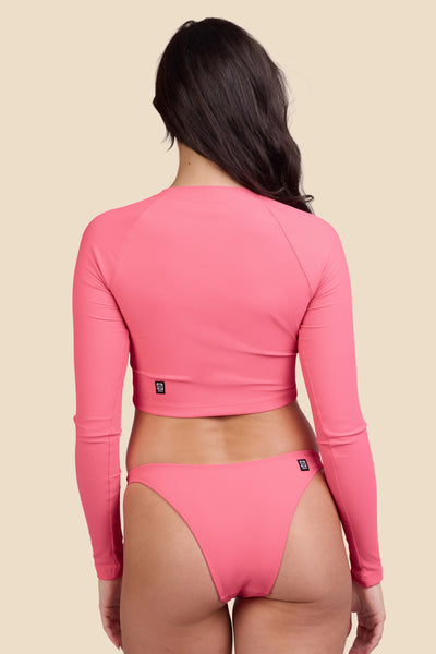 Female model wearing the Women's Moana Rashguard in the Tea Rose Ribbed solid, standing in front of a yellow background shown from the back view

|| Size M, Bust 32"  