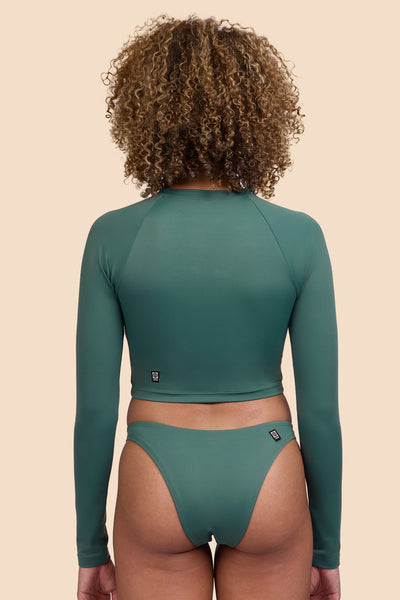 Female model wearing the Women's Moana Long Sleeve Rashgard in the Zucchini solid, standing in front of a yellow background shown from the back view

|| Size S, Bust 32.5"  