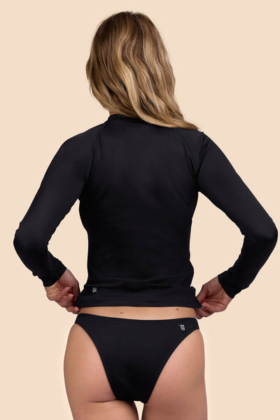 Female model wearing the Womens Noonan Rashguard in the Black solid, standing in front of a yellow background shown from the back view

|| Size S, Bust 33"  