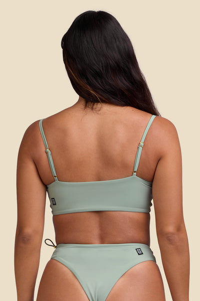 Female model wearing the Women's Zari Bikini Top in the Algae solid, standing in front of a yellow background shown front the back view

|| Size S, Bust 34"  