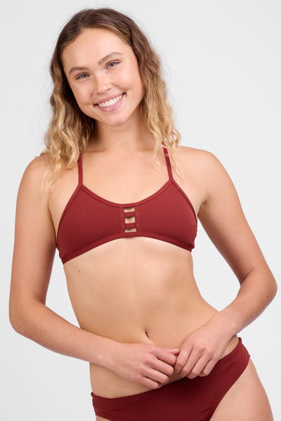 Female model wearing the Women’s Tomcat Bikini Tip in the Paprika solid, standing in front of a grey background, shown from front view. 
