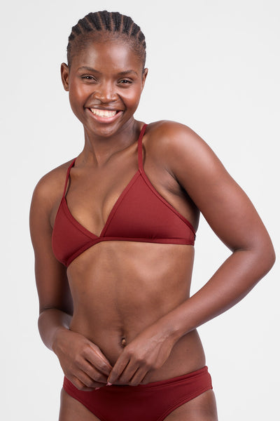 Female model wearing the Women’s Triangle Bikini Tip in the Paprika solid, standing in front of a grey background, shown from front view. 
