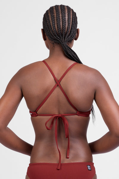 Female model wearing the Women’s Triangle Bikini Tip in the Paprika solid, standing in front of a grey background, shown from back view. 
