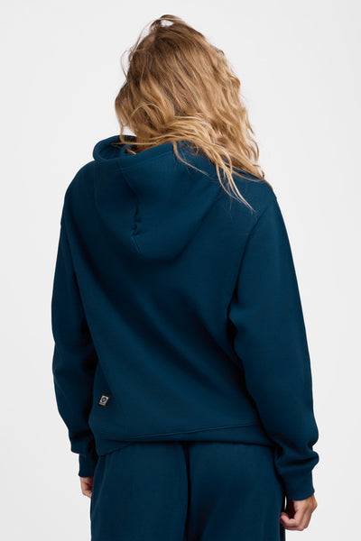 Female model wearing the Women's Lana Hoodie in the Indigo solid, standing in front of a grey background, shown from the back view

|| Size S, Bust 31.5"  