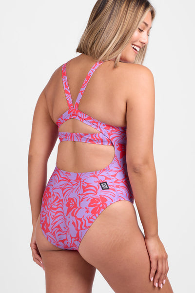 Female model wearing the Women's Caroline One Piece Swimsuit in the Sundara print, standing in front of a grey background, shown from the back view. 