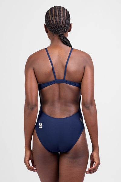 Female model wearing the Women's Chevy Tiger One Piece Swimsuit in the Navy solid, standing in front of a grey background, shown from the back view