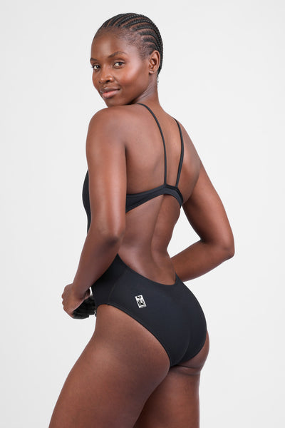 Female model wearing the Women's Chevy Tiger One Piece Swimsuit in the Black solid, standing in front of a grey background, shown from the side view
