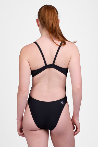 
Female model wearing the Women’s Christie One Piece Swimsuit in the Black solid, standing in front of a grey background, shown from back view. 
